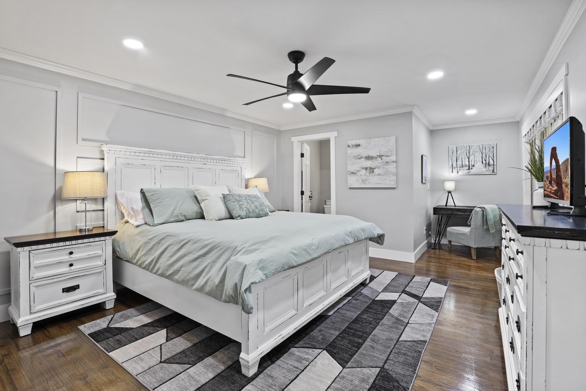 King bedroom with white bedframe, desk, and gray paneled walls