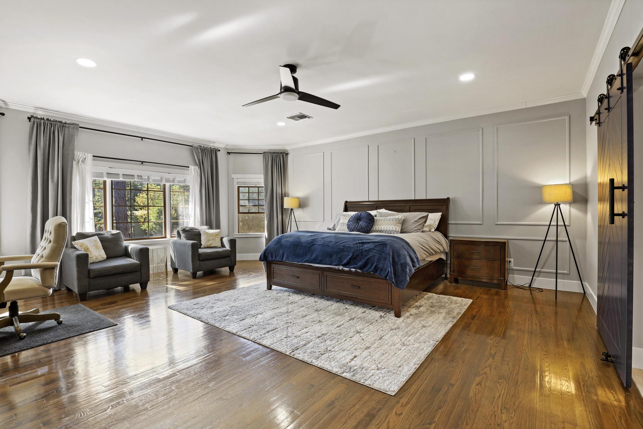 Large primary suite with seating area, blue bedding, and wide wood floors