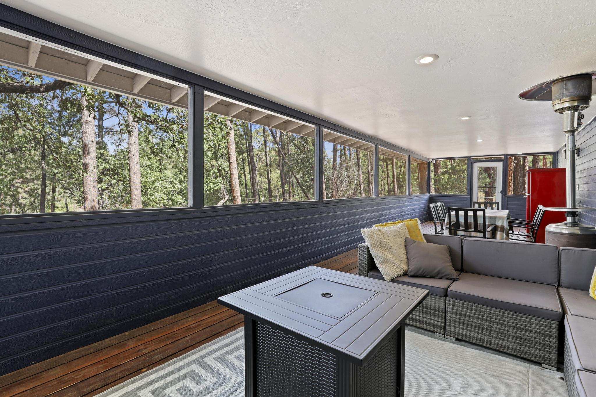 Screened porch with lounge seating, dining table, and pine views
